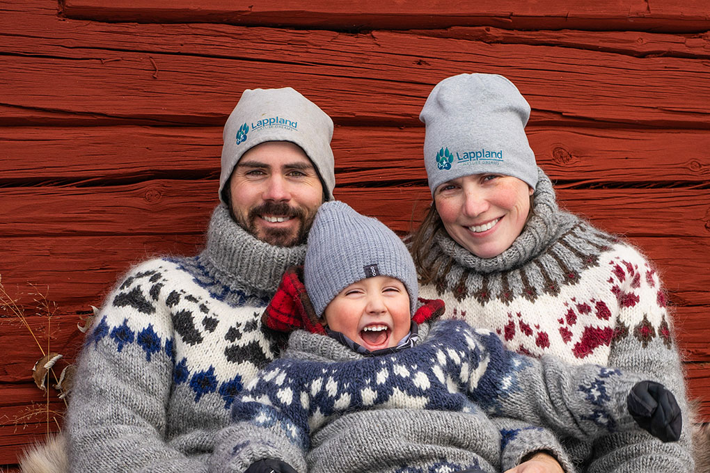 A family picture of Raphael & Yvonne and their son Joël in front of a dark red wall.